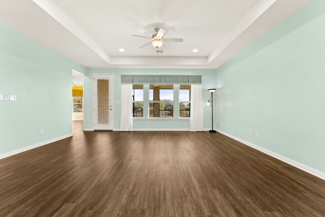 unfurnished living room with ceiling fan, a raised ceiling, and dark wood-type flooring