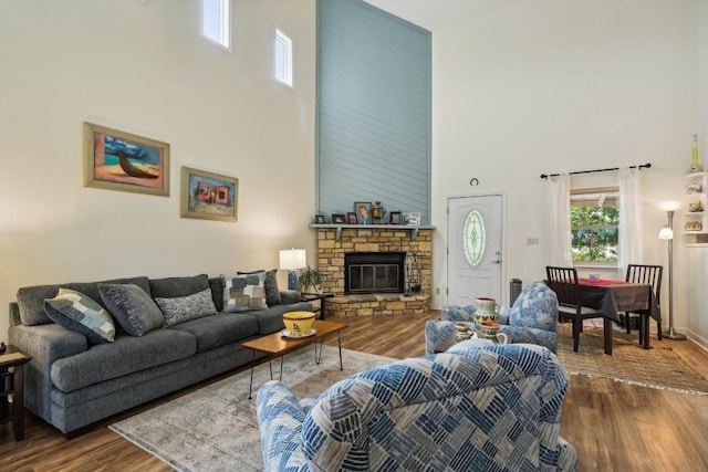 living room with a high ceiling, hardwood / wood-style flooring, and a stone fireplace