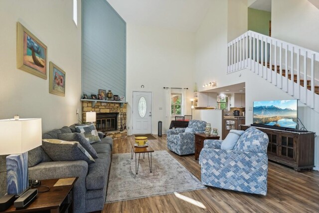 living room featuring hardwood / wood-style flooring, a stone fireplace, and a towering ceiling