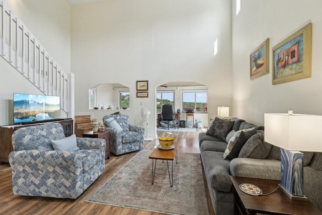 living area with stairway, arched walkways, a high ceiling, and wood finished floors