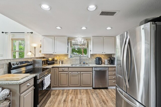 kitchen featuring visible vents, light wood-style flooring, a sink, stainless steel appliances, and backsplash