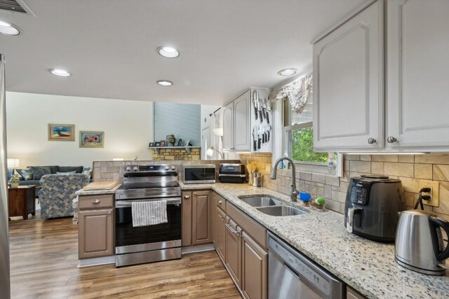 kitchen with visible vents, light wood-style flooring, a sink, tasteful backsplash, and stainless steel appliances