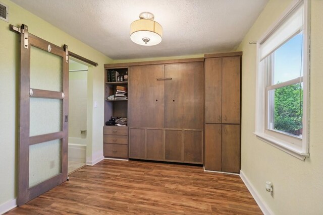 unfurnished bedroom featuring a textured ceiling, wood finished floors, a barn door, a closet, and baseboards