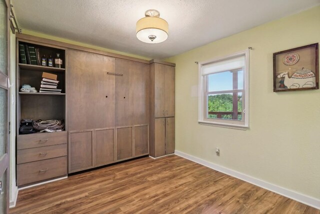 bedroom with wood finished floors, baseboards, a closet, and a textured ceiling