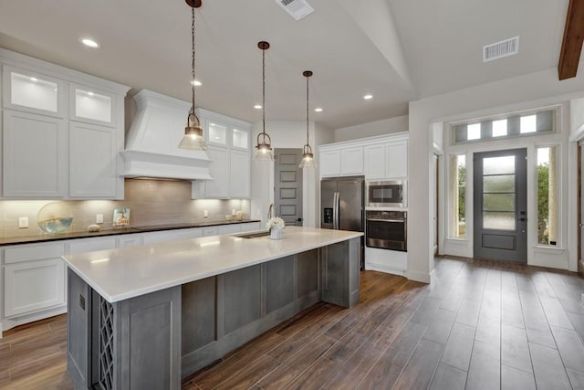 kitchen featuring custom range hood, stainless steel appliances, sink, white cabinetry, and an island with sink