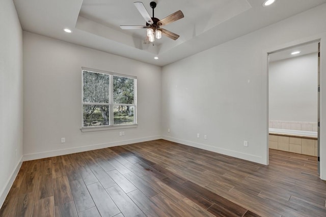 unfurnished room featuring dark hardwood / wood-style floors, ceiling fan, and a raised ceiling