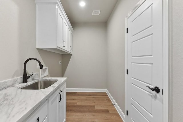 laundry room with electric dryer hookup, cabinets, sink, and light hardwood / wood-style floors