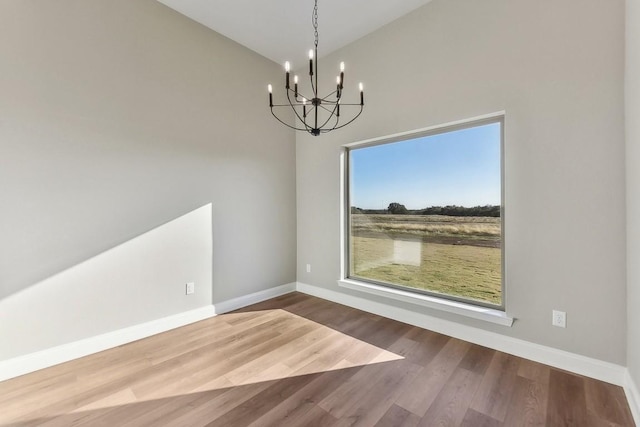 unfurnished dining area featuring hardwood / wood-style floors, lofted ceiling, and an inviting chandelier