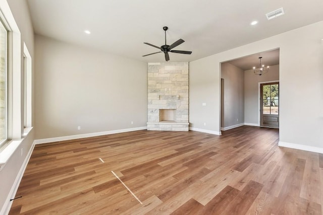 unfurnished living room with a fireplace, wood-type flooring, and ceiling fan with notable chandelier