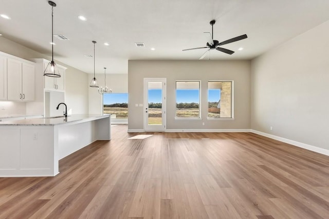 kitchen with white cabinetry, light stone counters, pendant lighting, ceiling fan with notable chandelier, and light wood-type flooring