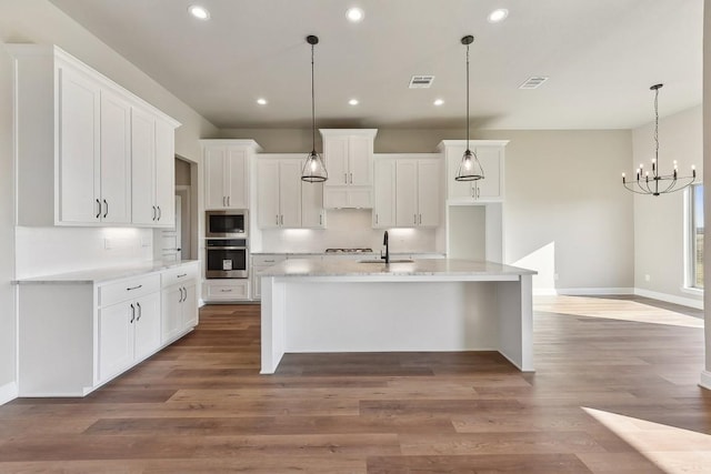 kitchen featuring white cabinets, hanging light fixtures, a kitchen island with sink, and appliances with stainless steel finishes