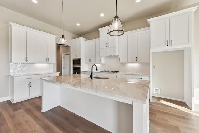 kitchen featuring stainless steel appliances, sink, pendant lighting, white cabinets, and an island with sink