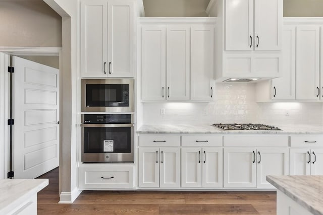 kitchen featuring light stone countertops, backsplash, stainless steel appliances, white cabinets, and hardwood / wood-style floors