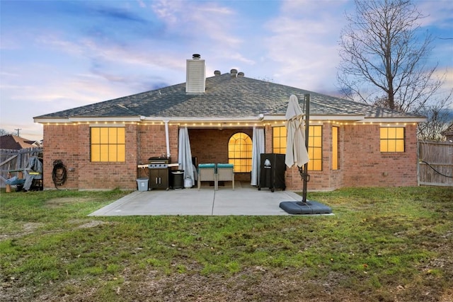 back house at dusk with a patio area and a yard