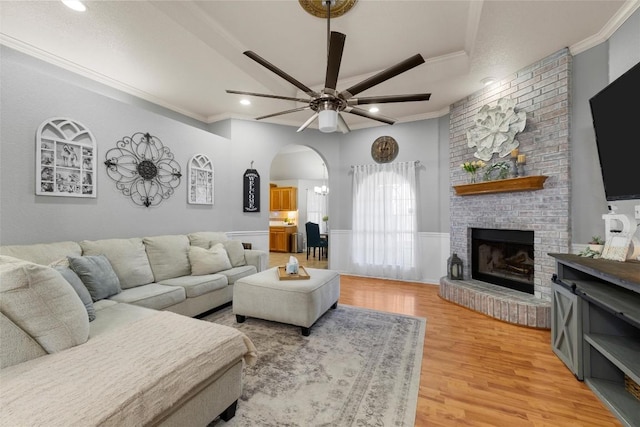 living room with a fireplace, ceiling fan, crown molding, and light wood-type flooring