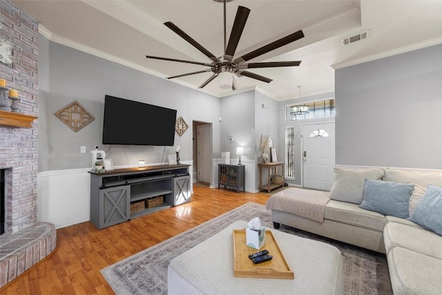 living room featuring crown molding, a fireplace, ceiling fan, and light hardwood / wood-style floors