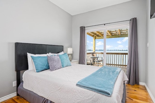 bedroom featuring access to outside, hardwood / wood-style floors, and a water view