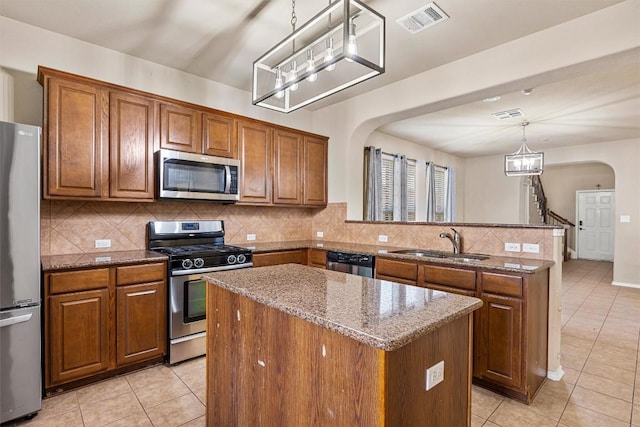 kitchen featuring light stone counters, stainless steel appliances, sink, pendant lighting, and a kitchen island