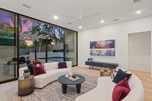 living room with ceiling fan, floor to ceiling windows, and light hardwood / wood-style flooring