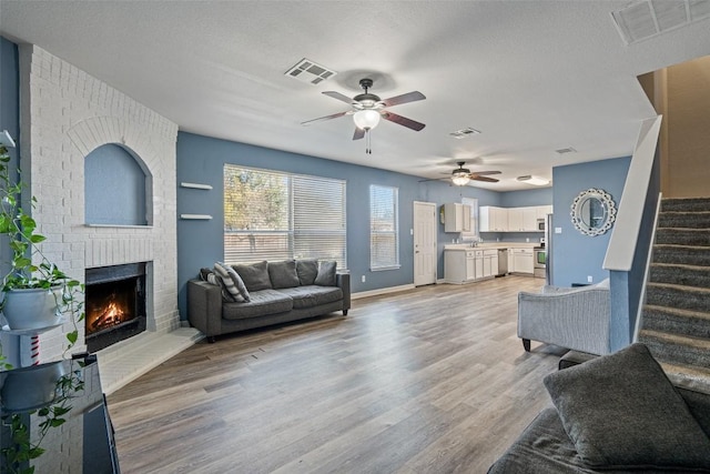 living room featuring a textured ceiling, ceiling fan, light wood-type flooring, and a fireplace