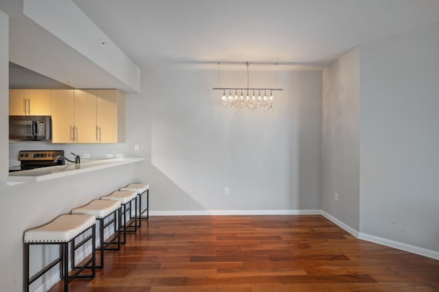 kitchen with dark wood-type flooring, a kitchen breakfast bar, electric range, cream cabinetry, and a notable chandelier