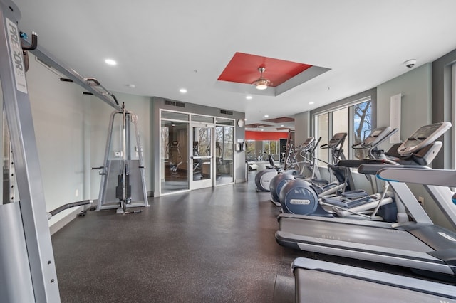 exercise room with a tray ceiling, a wealth of natural light, and ceiling fan