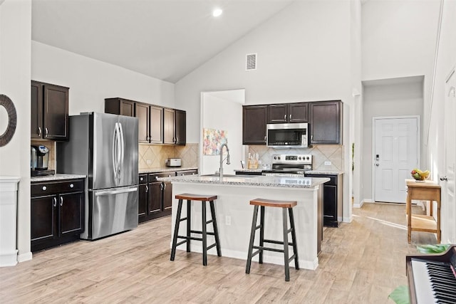 kitchen with sink, a breakfast bar, high vaulted ceiling, stainless steel appliances, and a center island with sink