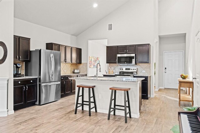 kitchen with appliances with stainless steel finishes, high vaulted ceiling, a sink, a breakfast bar area, and backsplash