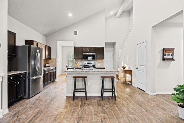 kitchen with a breakfast bar, tasteful backsplash, a kitchen island with sink, light stone counters, and stainless steel appliances