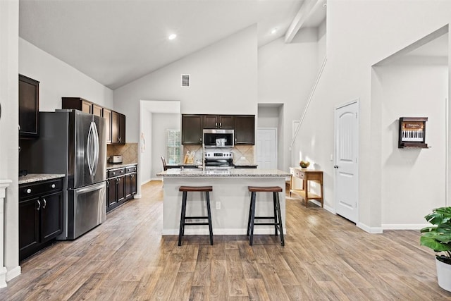 kitchen featuring appliances with stainless steel finishes, a kitchen bar, backsplash, light wood-type flooring, and high vaulted ceiling