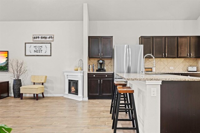 kitchen featuring dark brown cabinetry, a breakfast bar area, light hardwood / wood-style flooring, stainless steel fridge, and backsplash