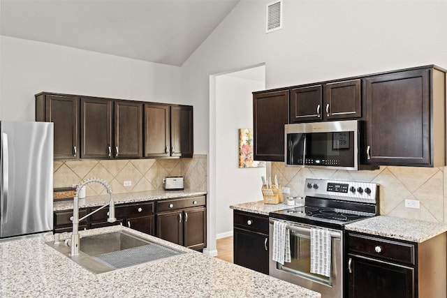 kitchen with dark brown cabinetry, sink, vaulted ceiling, and stainless steel appliances