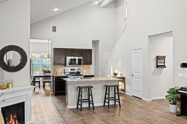 kitchen with appliances with stainless steel finishes, high vaulted ceiling, an island with sink, a kitchen breakfast bar, and backsplash
