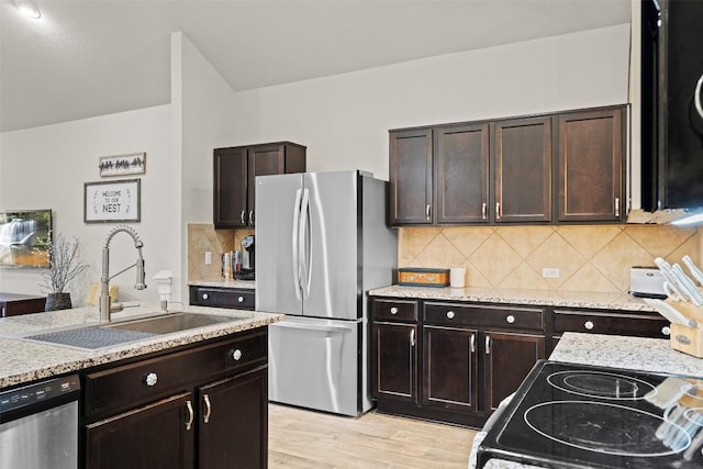 kitchen with appliances with stainless steel finishes, a sink, light wood finished floors, backsplash, and dark brown cabinets