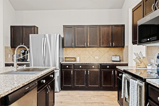 kitchen with appliances with stainless steel finishes, dark brown cabinets, sink, and light hardwood / wood-style flooring