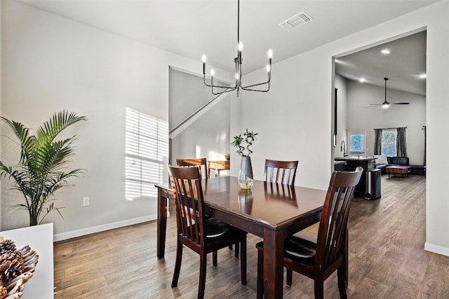 dining area featuring hardwood / wood-style flooring, vaulted ceiling, and ceiling fan with notable chandelier