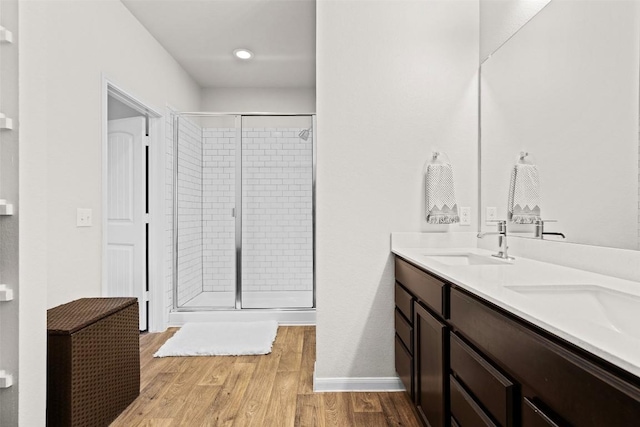 full bath with a stall shower, wood finished floors, double vanity, and baseboards