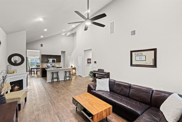 living room with light hardwood / wood-style floors, high vaulted ceiling, and ceiling fan