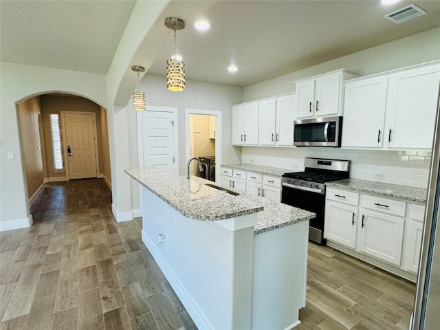 125 Millsaps Ct, Bastrop, TX 78602 - kitchen featuring appliances with stainless steel finishes, a sink, arched walkways, white cabinetry, and a center island with sink