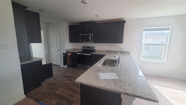 kitchen with kitchen peninsula, appliances with stainless steel finishes, dark hardwood / wood-style flooring, light stone countertops, and sink