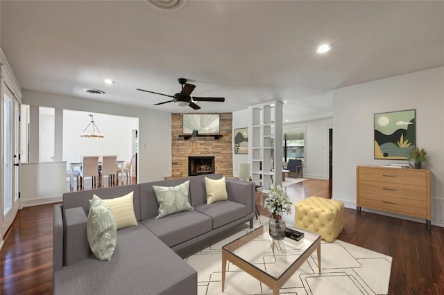 living room featuring a stone fireplace, recessed lighting, dark wood-type flooring, and ornate columns