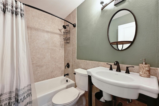 bathroom featuring shower / bath combination with curtain, toilet, a textured wall, and a sink