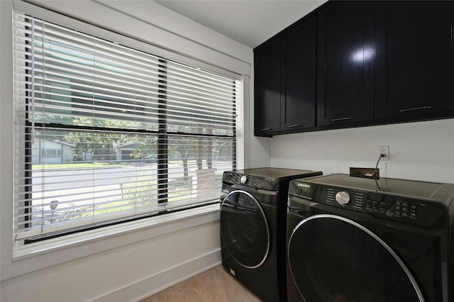 clothes washing area featuring light tile patterned floors, cabinet space, baseboards, and washing machine and clothes dryer