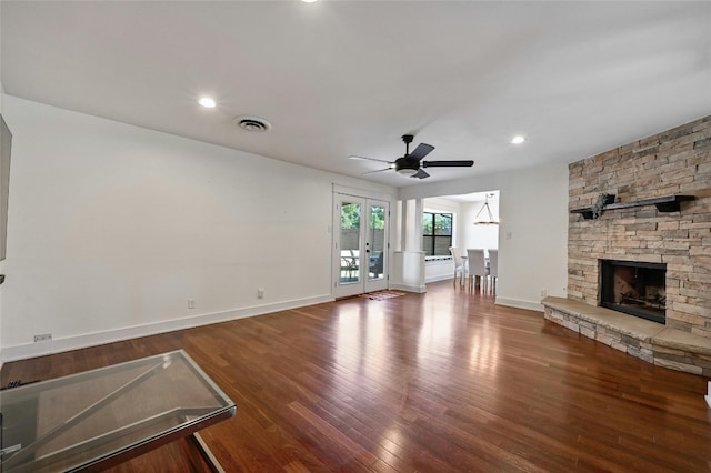 unfurnished living room with visible vents, a stone fireplace, baseboards, and wood finished floors