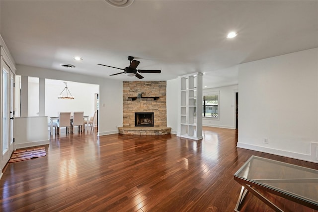 living room featuring dark wood finished floors, a fireplace, decorative columns, baseboards, and ceiling fan