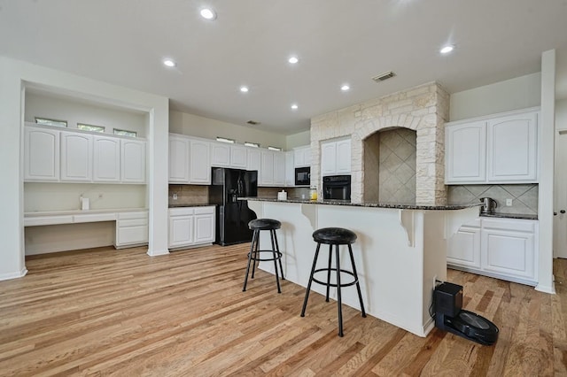 kitchen featuring light wood-type flooring, black appliances, dark stone countertops, white cabinetry, and a breakfast bar area