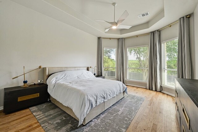 bedroom with multiple windows, hardwood / wood-style floors, a tray ceiling, and ceiling fan