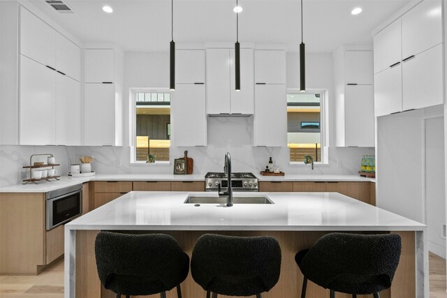 kitchen with white cabinetry, a kitchen island with sink, and stainless steel microwave