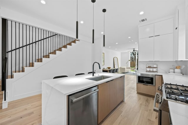 kitchen featuring appliances with stainless steel finishes, sink, a center island with sink, white cabinetry, and hanging light fixtures