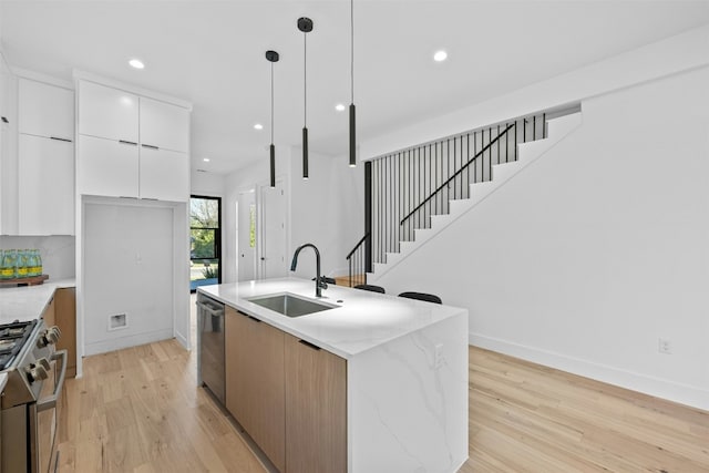 kitchen featuring light stone countertops, sink, stainless steel appliances, a center island with sink, and white cabinets